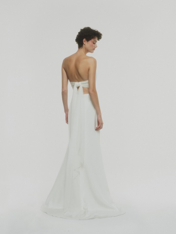 Modernes rückenfreies Bustier-Brautkleid mit Schleifenband und fließendem Rock, Braut mit kurzen dunklen Locken vor weißem Hintergrund