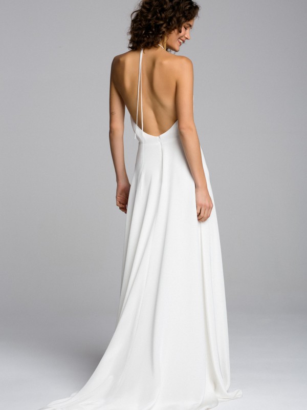 Modernes rückenfreies Brautkleid in Weiß mit Halterneck und langem Bindeband im Nacken, fließender Rock, Braut mit lockigem kurzen Haar vor hellem Hintergrund