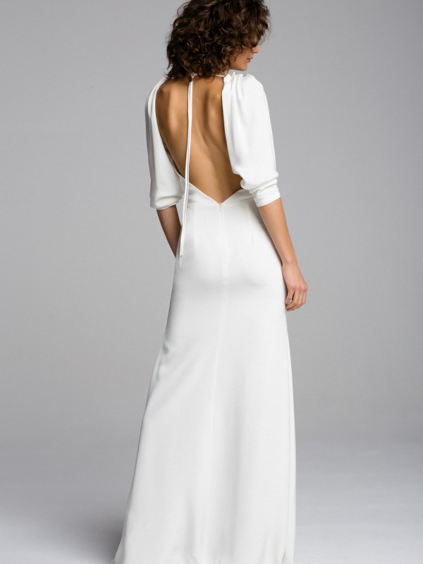 Modernes rückenfreies Brautkleid mit langen Ärmeln, tiefem Rückenausschnitt und feinem Bindeband im Nacken, schlichtes Design vor neutralem Hintergrund