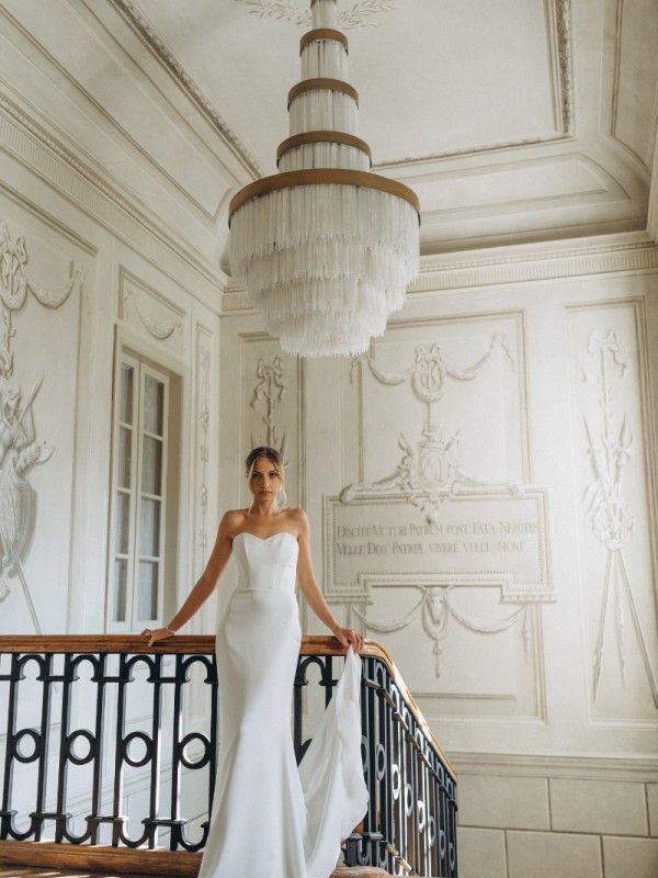 Clean-Brautkleid mit modernem Herzausschnitt, glatte und schlichte Silhouette, Braut mit elegantem Zug vor klassischer Kulisse